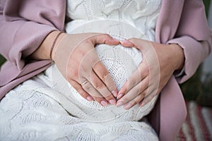 Motherâ€™s hands in a shape of heart holding a belly. Close up pregnant woman`s belly. Prenancy and maternity concept.