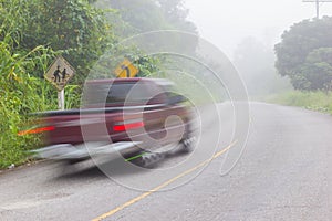 Motion blur of car on road on foggy morning along green tree lin