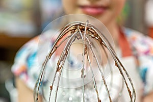 motion blur effect photo of little kid girl cooking and tastes licks chocolate dough from a whisk for whipping dough at home. dome