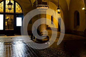 Motion blur of man smoking next to the columns at sukiennice Cloth Hall at night, with lamp lighting overhead. Krakow, Poland.