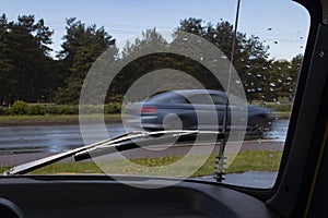 Traffic watched through the windshield of a vintage car with a chrome wiper and antenna