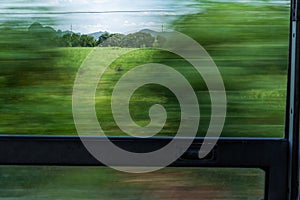 Motion blur train window view with green trees and sky
