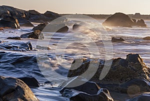 Motion blur wave breaking rocky shoreline sunrise