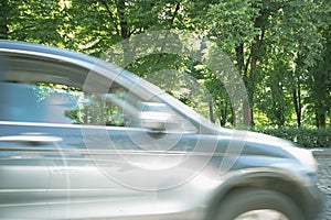 Motion blurred fast moving car. Background of green trees