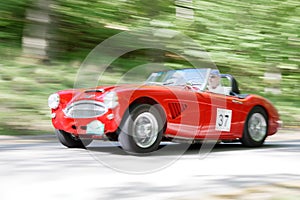 Motion blurred red color Austin Healey 3000 MKII classic car from 1961 driving in a country road