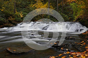 Motion-blurred water of Dingmans Creek surrounded by fall color