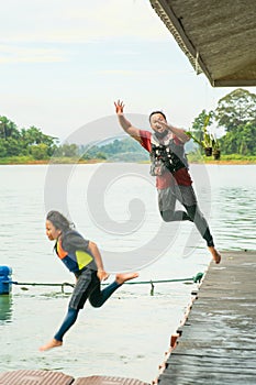 Motion of father and daughter jumping into the lake from the deck