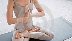 Motion past lady yoga practitioner in new beige tracksuit sitting in lotus position with namaste on mat in light studio