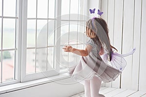 Motion photo. Nice little girl in the fairy tale wear going to the windows to look what`s outside