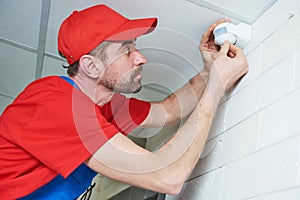 Worker installing or adjusting motion sensor detector on the ceiling