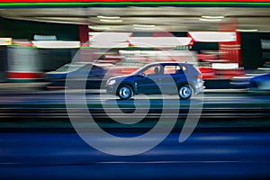 Motion shot of a black car driving fast down a road near an illuminated gas station