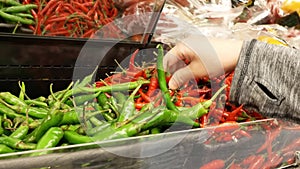 Motion of woman`s hand picking green and red hot pepper inside Superstore