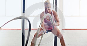 Motivate your mind and your body will follow. a young woman working out with battle ropes in a gym.