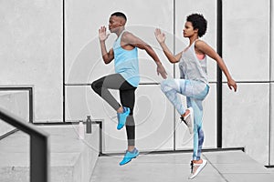 Motivated active ethnic couple run up stairs together, jump highly, train climbing staircase in city, wear comfortable