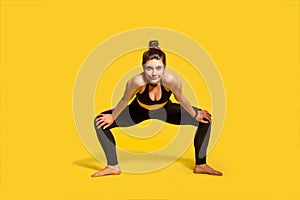 Motivated assertive gymnast girl with hair bun in tight sportswear squatting and spreading legs to stretch muscles