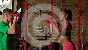 Motivated athletic black female boxer striking focus mitt during training at gym