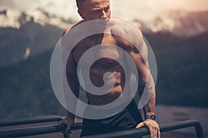 Motivated athletic man does bodyweight push ups at mountains area outdoor gym.