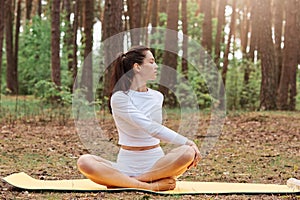 Motivated athletic positive woman in white leggins and top, practicing yoga, sitting in lotus pose and turning back, flexibility