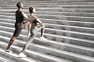 Motivated Black Couple Warming Up Muscles Before Jogging Outdoors On Urban Stairs