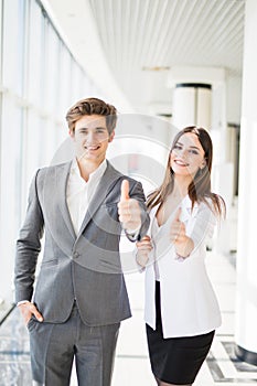 Motivated businessman and woman giving a thumbs up gesture of approval and success as they pose side by side giving the camera big