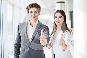 Motivated businessman and woman giving a thumbs up gesture of approval and success as they pose side by side giving the camera big