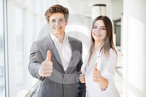 Motivated businessman and woman giving a thumbs up gesture of approval and success as they pose side by side giving the camera big