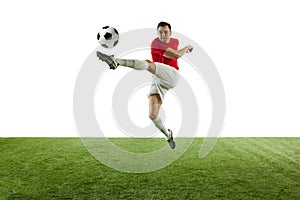 Motivated and competitive male football player hitting ball in jump, during training session of stadium isolated on