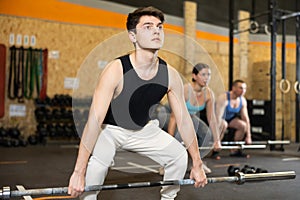 Motivated CrossFit male athlete lifting heavy body bar or barbell during group training in gym. Functional training