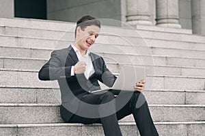 Motivated expression young business man sitting on stairs  working with his laptop