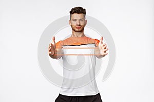 Motivated good-looking sexy male athlete workout using gym equipment, stretch resistance band with hands and look camera