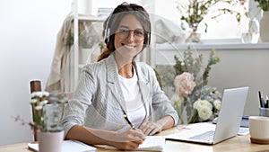 Motivated millennial female remote worker doing paperwork using laptop headphones