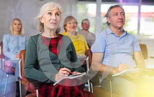 Motivated older woman listening to lecture in group auditorium