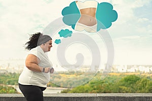 Motivated overweight woman dreaming about slim body while running outdoors.