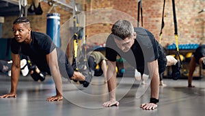 Motivated People Only. Caucasian man stretching his body while doing fitness TRX training exercises at industrial gym
