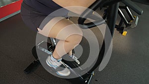 Motivated plump girl pedaling fast at exercise bike in the gym, active workout