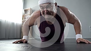 Motivated plump man in his 50s doing push-up with great effort, home training