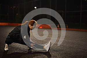 Motivated redhead female athlete stretching legs for warming up before urban fitness