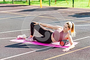 Motivated sporty woman training on mat outdoor summer day, using foam roller massager for relaxation, stretching spine