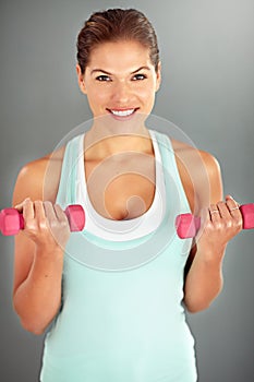 Motivated to reach her fitness goals. a young woman working out with dumbbells against a gray background.