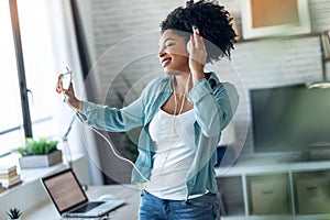 Motivated young afro woman listening to music with headphone while dancing in living room at home