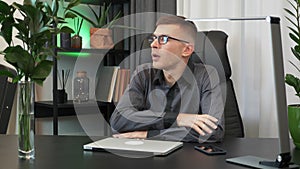 Motivated young man is closing laptop computer and finishing to work at workplace desk in the evening. Businessman in glasses fini