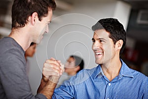 Motivating one another to success. Two business colleagues clasping hands and laughing in the office.