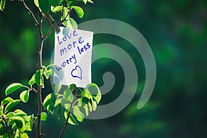 Motivating phrase love more worry less. On a green background on a branch is a white paper with a motivating phrase photo