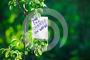 Motivating phrase You can change the world. On a green background on a branch is a white paper with a motivating phrase