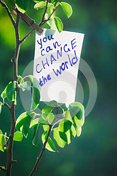 Motivating phrase You can change the world. On a green background on a branch is a white paper with a motivating phrase.