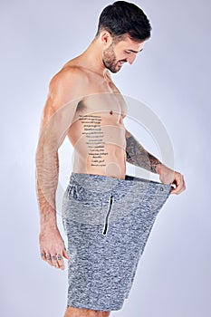 Motivation, diet and weight loss, man checking pants size change from workout and healthy lifestyle on studio background
