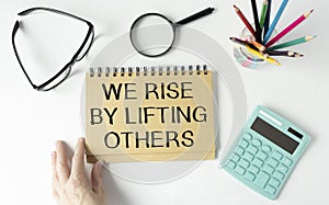 motivation life quote on notepad - We Rise by Lifting Others