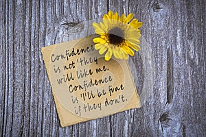 Motivational on brown note with gerbera yellow flower on wooden surface.