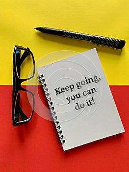 Motivational and inspirational concept - Keep going, you can do it. With glasses, pen, yellow and red background