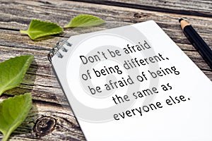 Motivational and inspirational quote on notepad with green leaf on wooden desk.